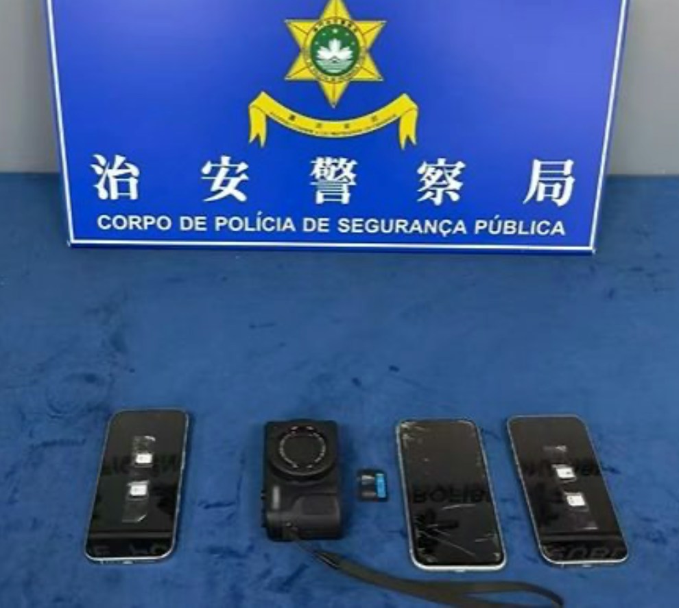 The seized camera and phones displayed at a Macau police station, with the Public Security Police Force's sign behind. Photo: HK01