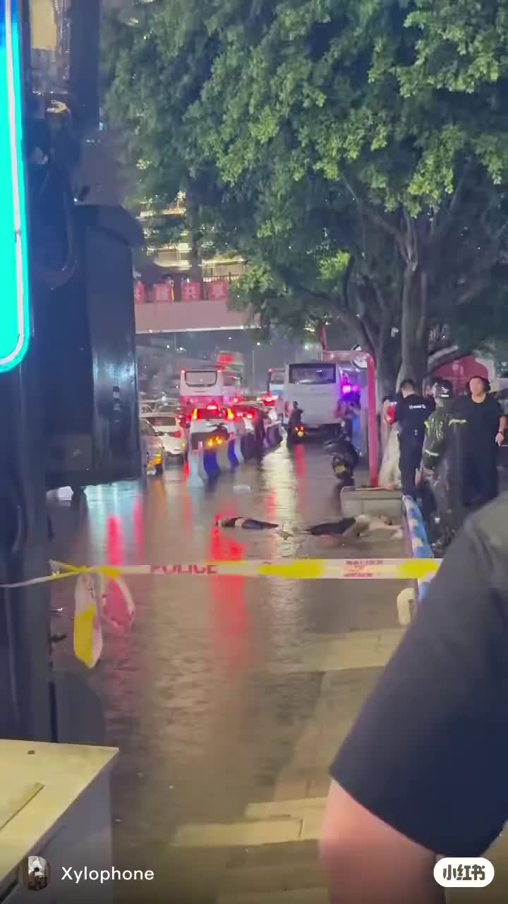 Police tape and emergency vehicles surround two people on a flooded Chongqing road
