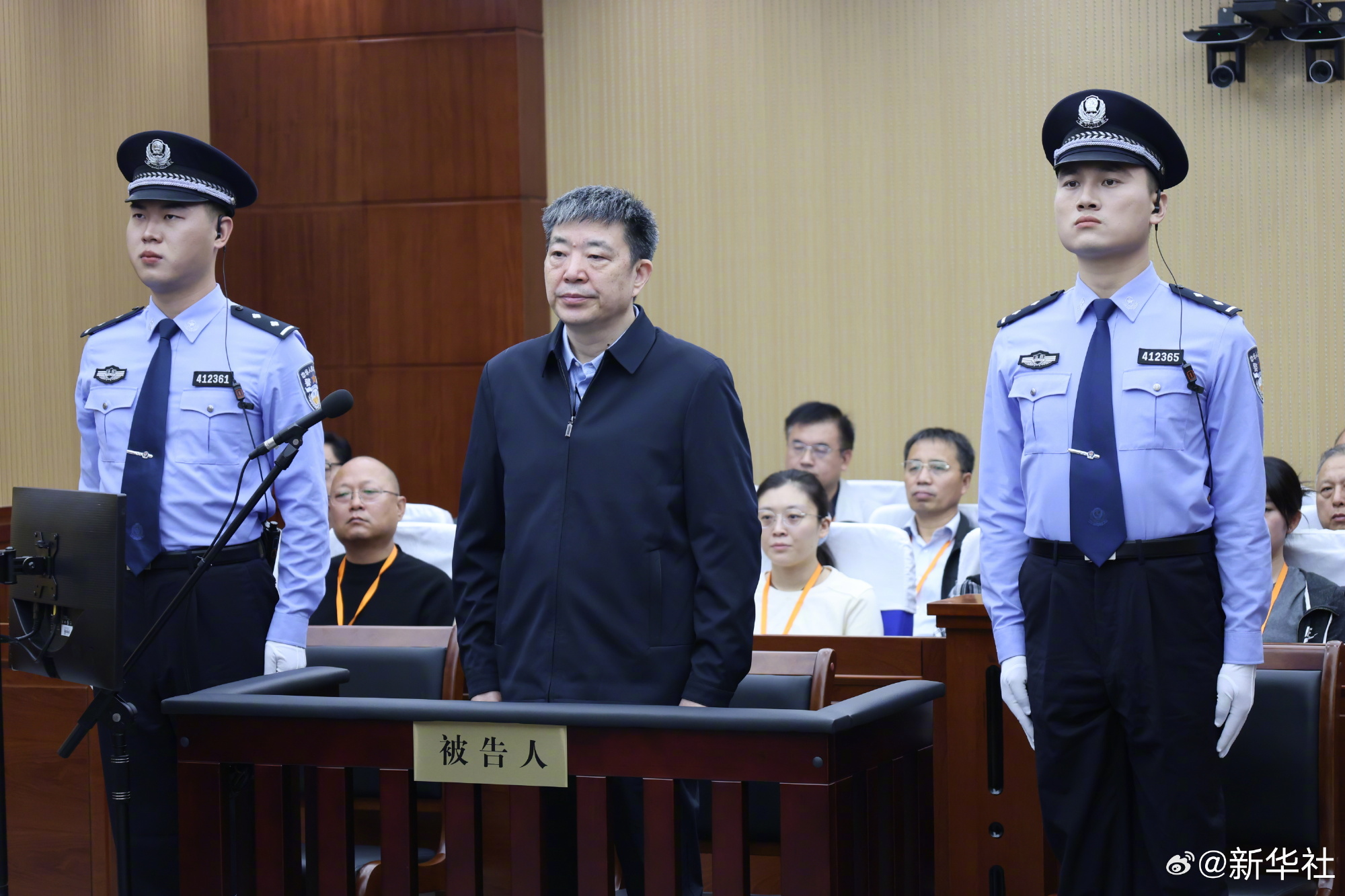 Zhou Xianwang stands in the defendants' dock of the Shangqiu Intermediate People's Court, flanked by bailiffs, at the verdict reading. Photo: @新华社