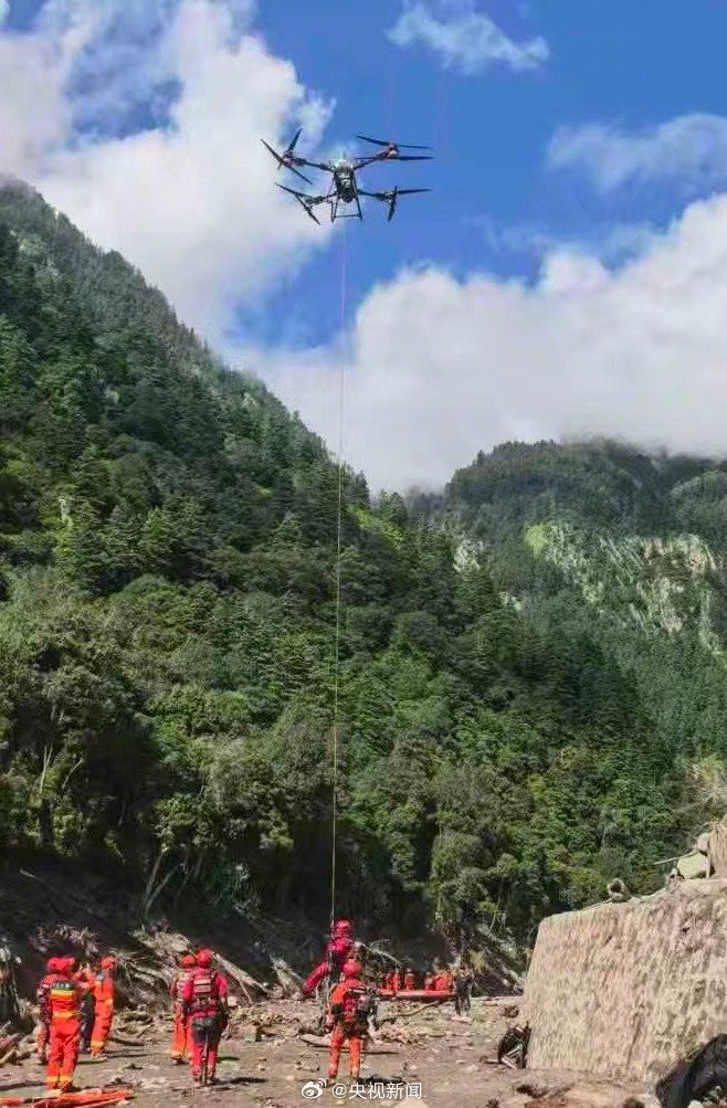 A heavy-lift drone hovers over rescue personnel gathered on rocky ground in a steep mountain valley. Photo: @央视新闻