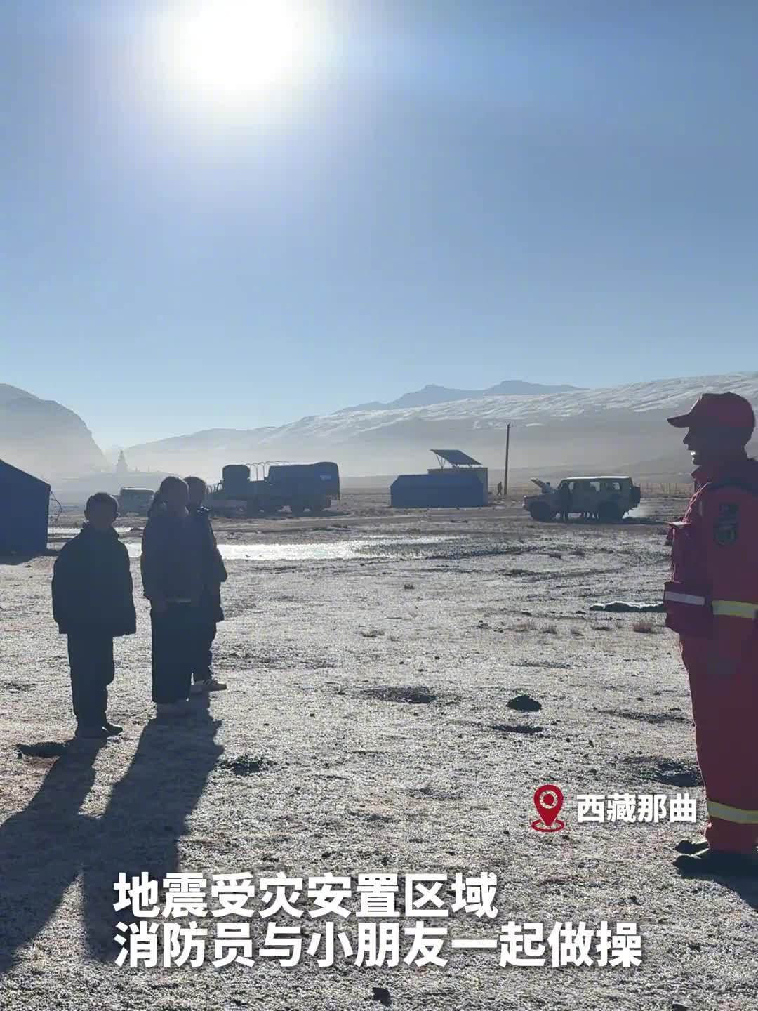 A video still from the resettlement area in Nagqu, Tibet: firefighters and children doing morning exercises together, with camp trucks and snow-capped mountains behind. Photo: @芥末Sep