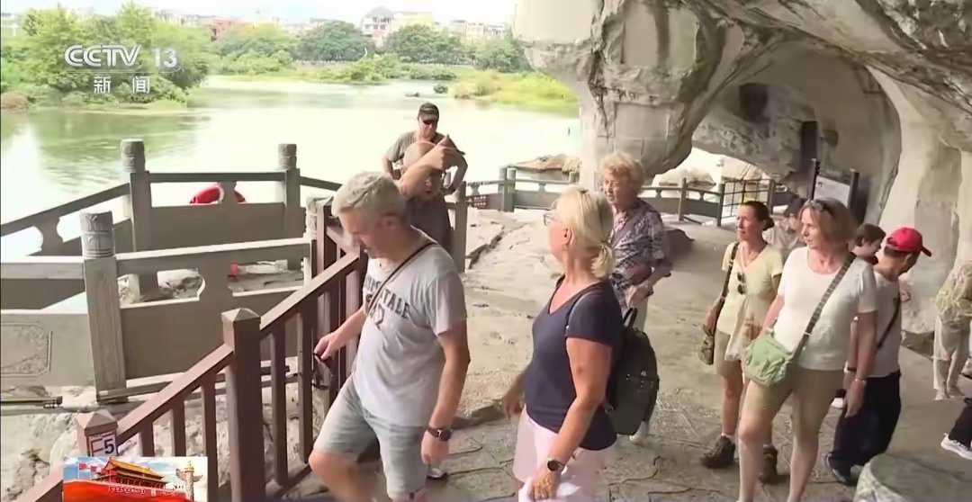 Foreign visitors walk a stepped path under a rock overhang at a scenic area in China, in a frame from a CCTV news broadcast. Photo: @天空菌