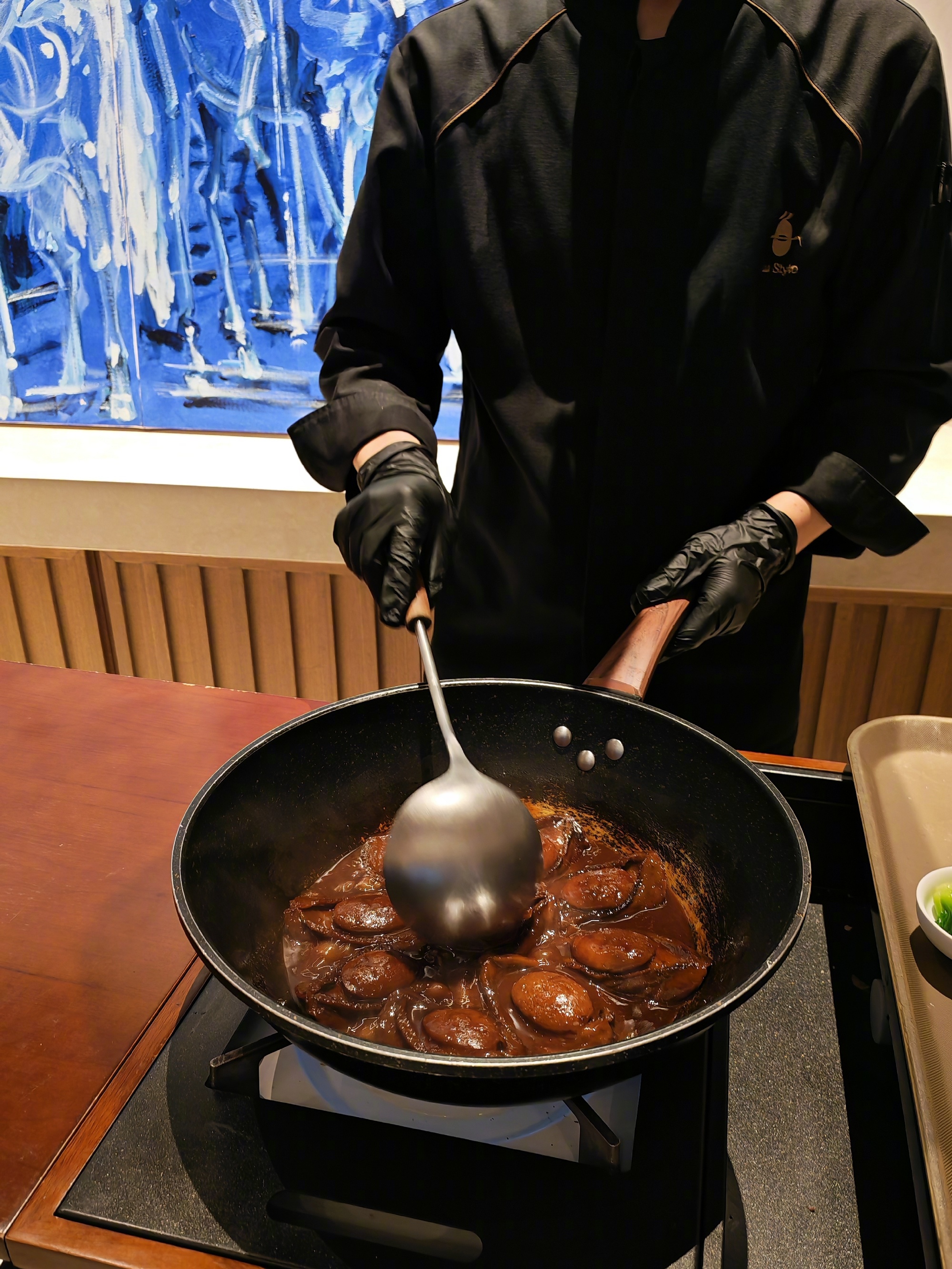 A chef in black and gold stirs a glossy braise in a black wok at Lu Style, a Lu cuisine restaurant in Beijing. Photo: @陈震同学
