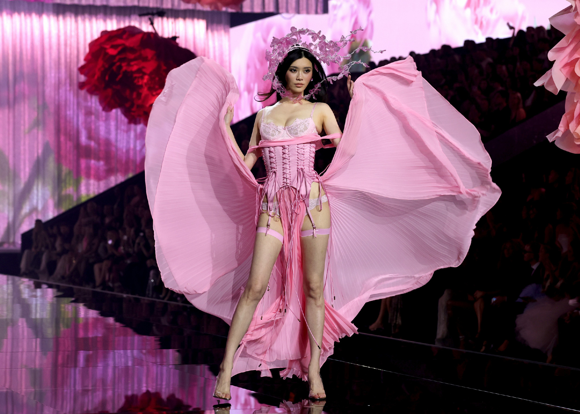 A model on the show's glossy black runway in a pink corset-style outfit with billowing fabric wings and a floral headpiece. Photo: @Houson猴姆