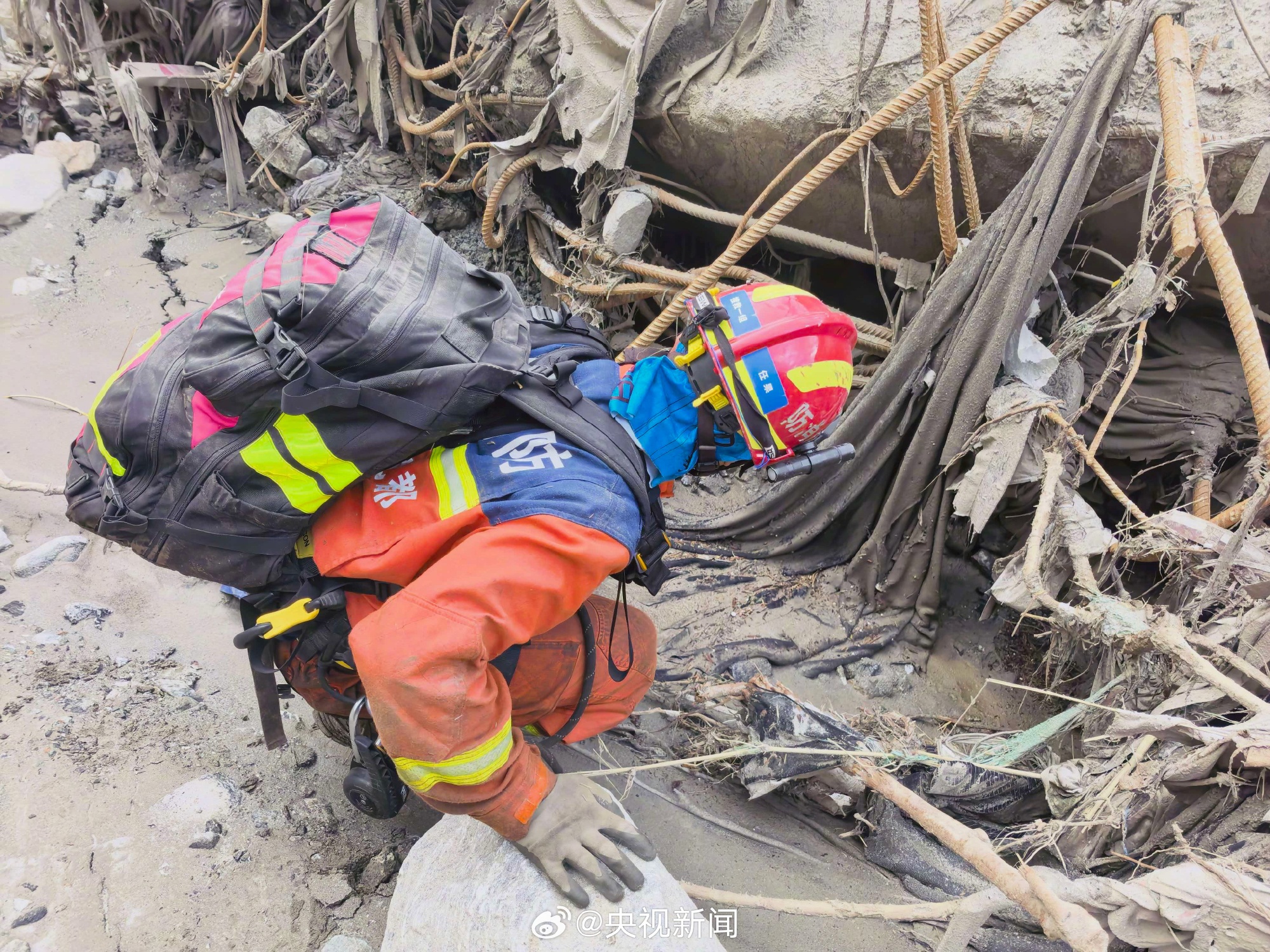 A rescue worker in fire-service uniform reaches into a gap beneath broken concrete at the Gyirong mudslide site. Photo: @央视新闻