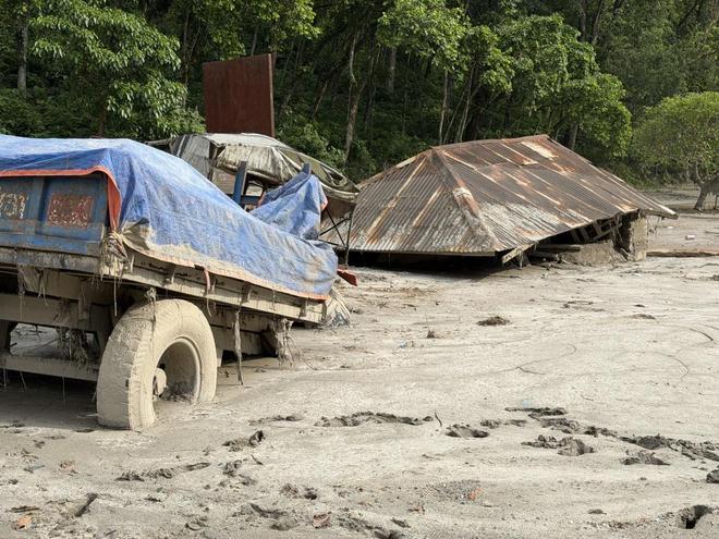 A truck sunk to its axles in dried mud beside a collapsed corrugated roof in the disaster zone. Photo: @头条新闻