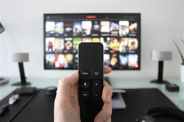 A hand holds a media remote in front of a television grid of streaming posters — the clutter the reform promises to simplify. Photo: @观察者网