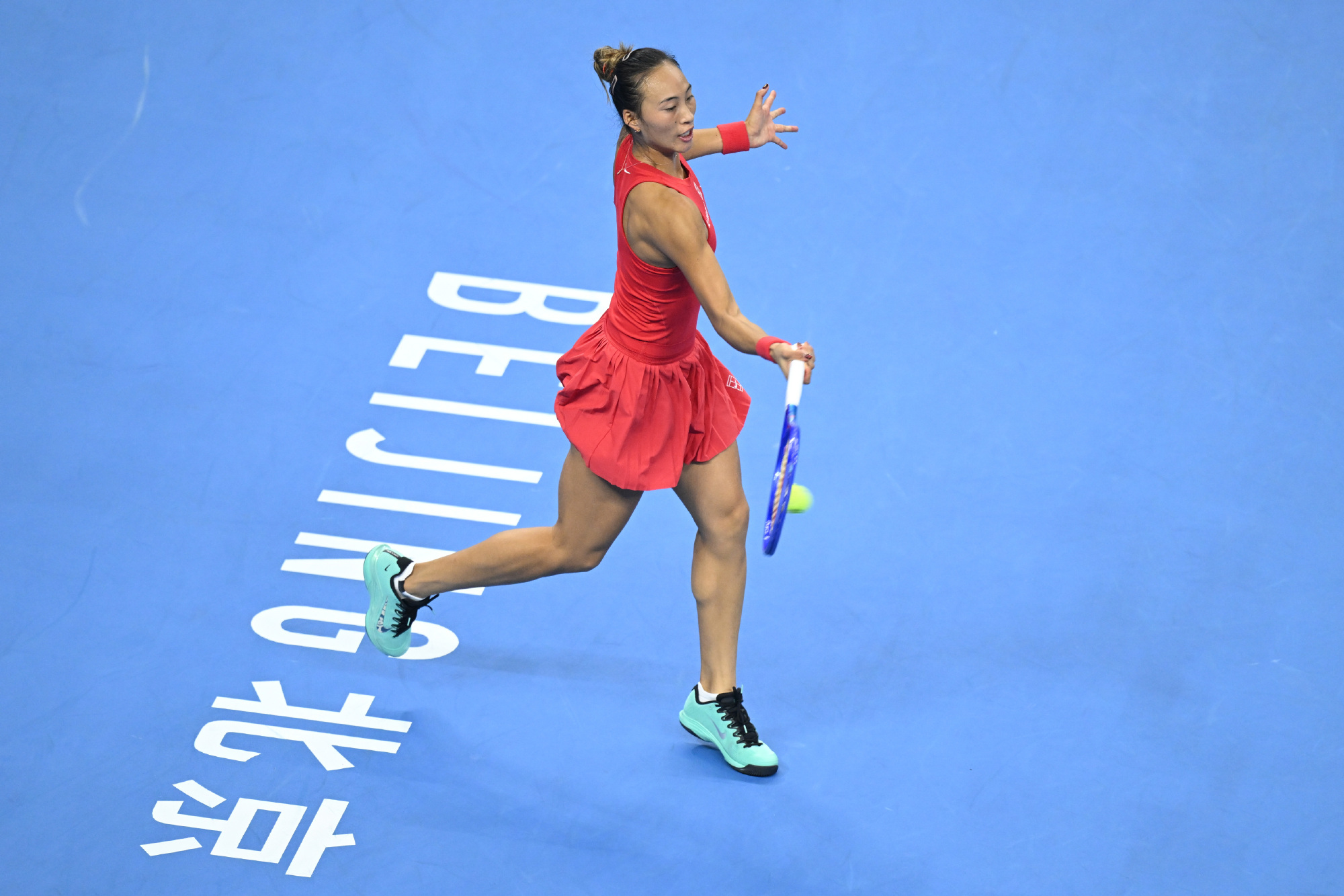 Zheng Qinwen in mid-swing on the blue court at the China Open, "Beijing" painted under her feet. Photo: @WTA国际女子网球协会