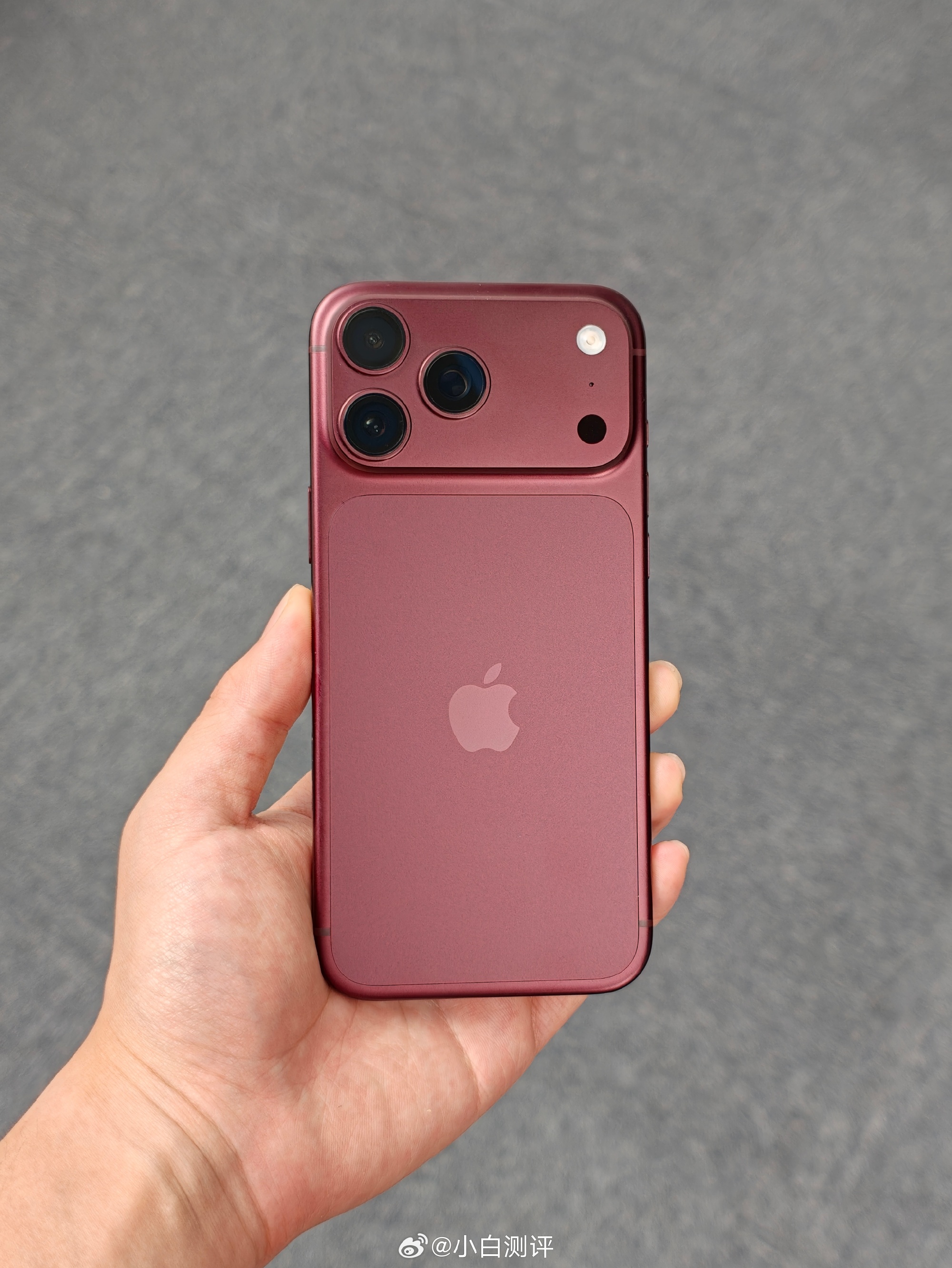 A hand holds a dark-red Apple handset in a hands-on photo from a Mate 90 versus iPhone 18 comparison post. Photo: @小白测评