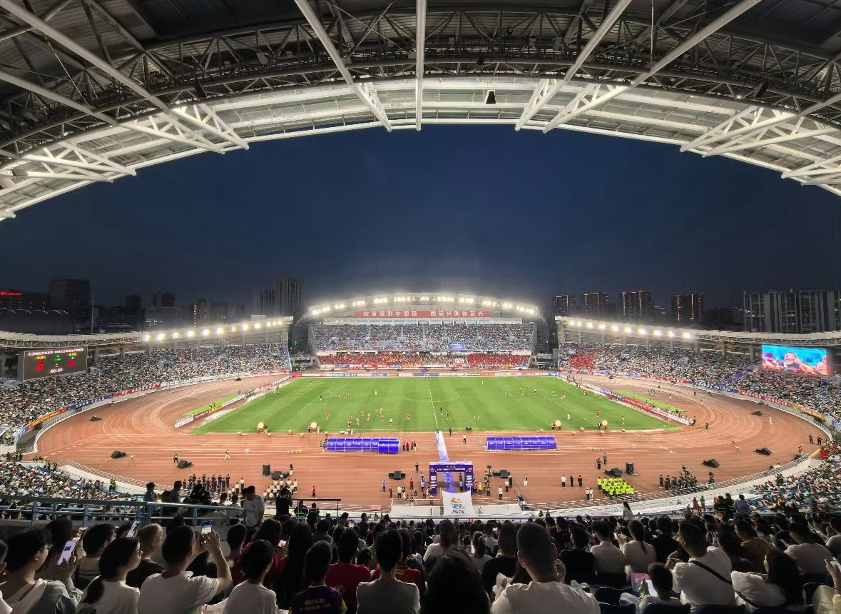 A packed stadium under lights during the Jiangsu City Football League final, with a banner reading "Sports strengthen the nation" across the far stand. Photo: @锦李小才女